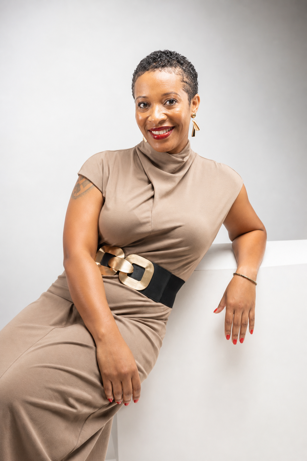 Lasheika Kassa, Founder and Principal Consultant of Fanik Consulting, seated in a tan dress with a gold-buckled belt